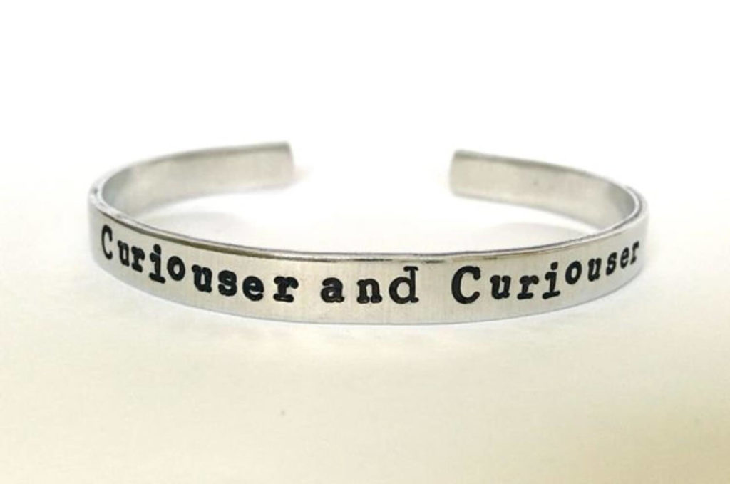 Metal bracelet with "Curiouser and Curiouser" stamped on it