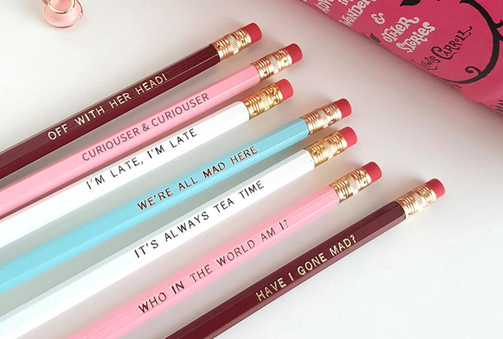 A collection of pink, white, burgundy, and teal pencils with various Alice in Wonderland quotes engraved on their sides