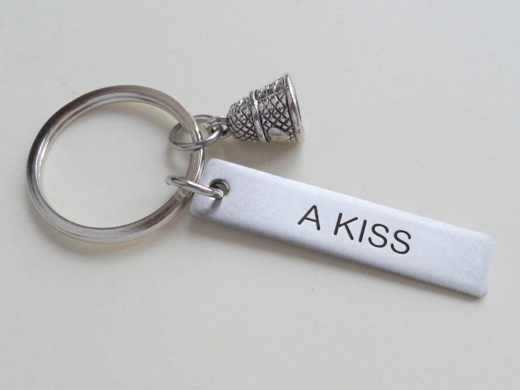 Keychain with a thimble charm and a metal bar that reads "A Kiss"