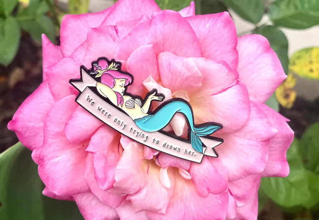 Mermaid shaped enamel pin with the words "We were only trying to drown her"