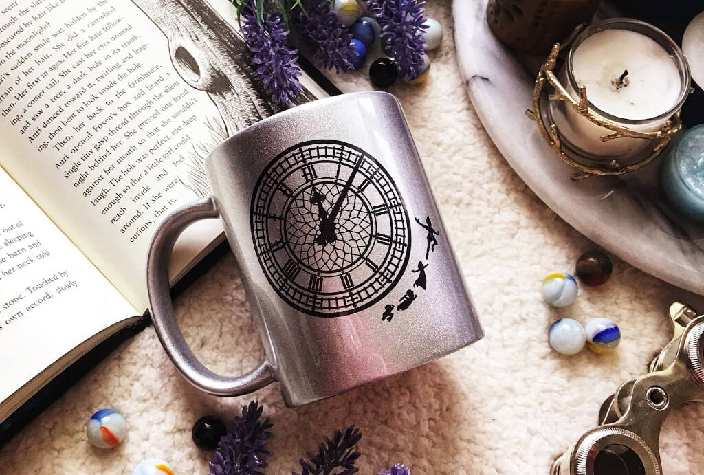 Silver mug decorated with a clock face and Peter, Wendy, John, and Michael flying beside it