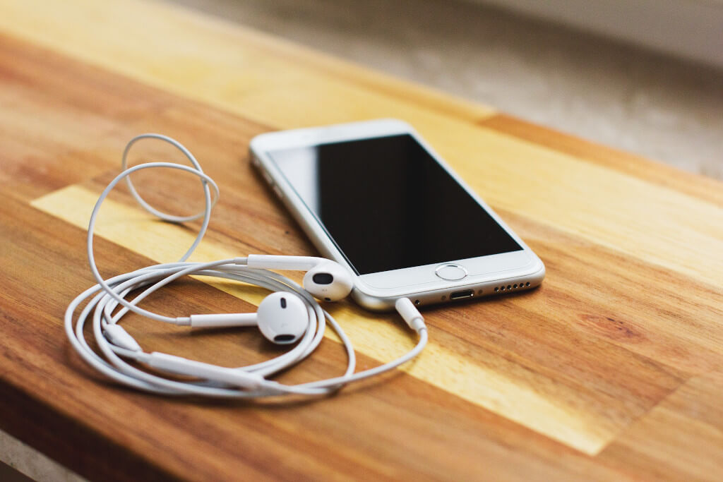 White phone and earbuds sitting on a wooden table