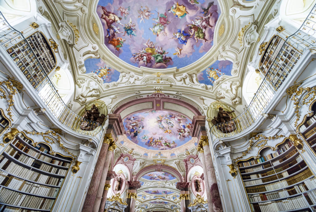 White walls filled with bookshelves and vibrant paintings on the ceiling in the Admont Abbey Library