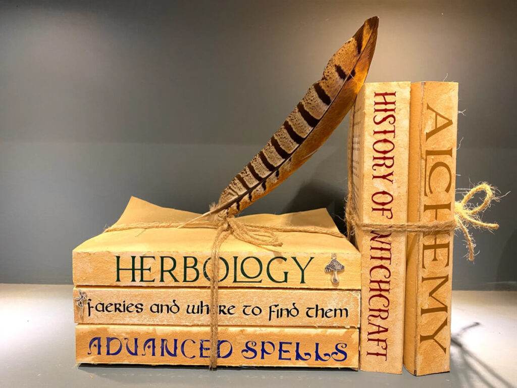 Stacked books tied with twine that say things like "Herbology" and "Alchemy" by TheMossyHare