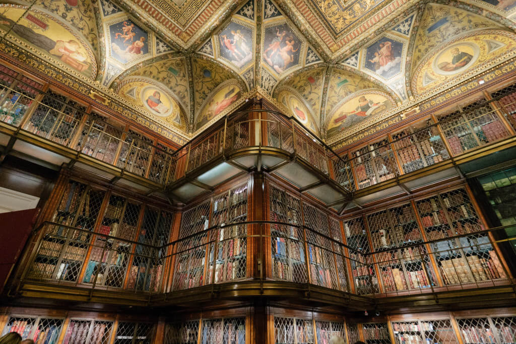 Bookshelves lining the walls and intricate ceiling mosaics of the Morgan Library in New York City
