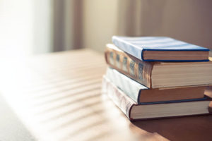 Four books piled up on a table with sunlight on them