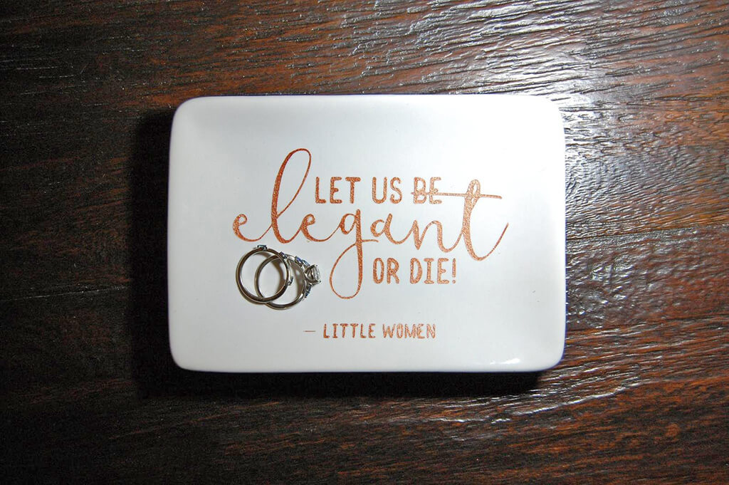 White rectangular dish with gold writing on it that says "Let us be elegant or die - Little Women" by Bunbury and Co