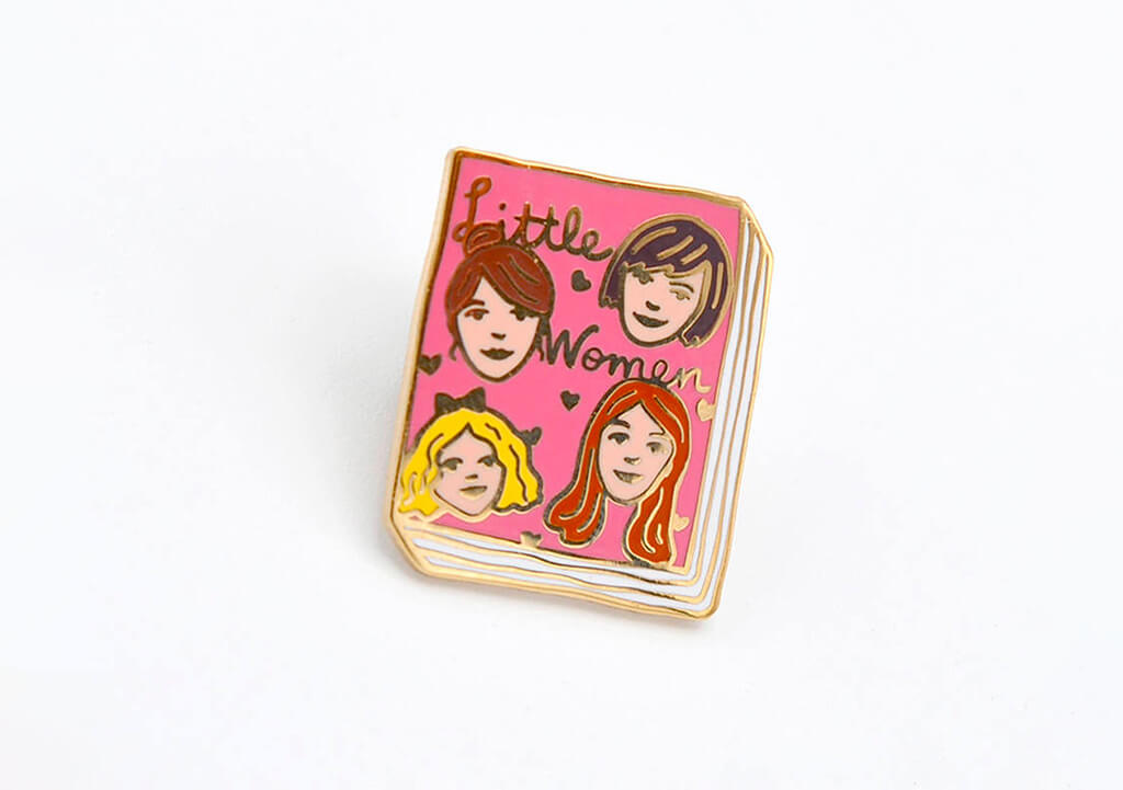 Pink book-shaped enamel pin with four women on the front and the words "Little Women". By Jane Mount
