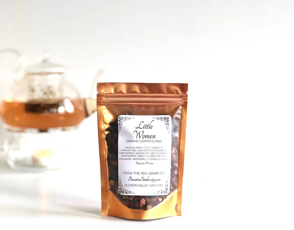 Gold package with see-through front showing loose leaf tea. Package says "Little Women". By BeauTea Studio