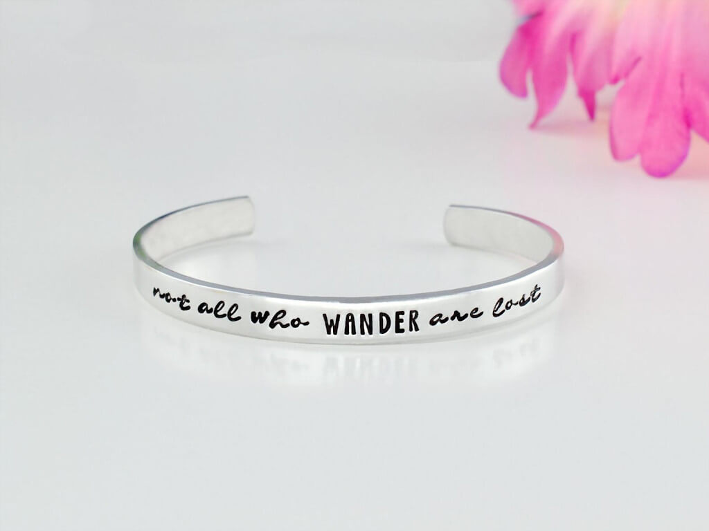Silver cuff bracelet with hand stamped letters that say "not all who wander are lost". By Wonderful Stamping