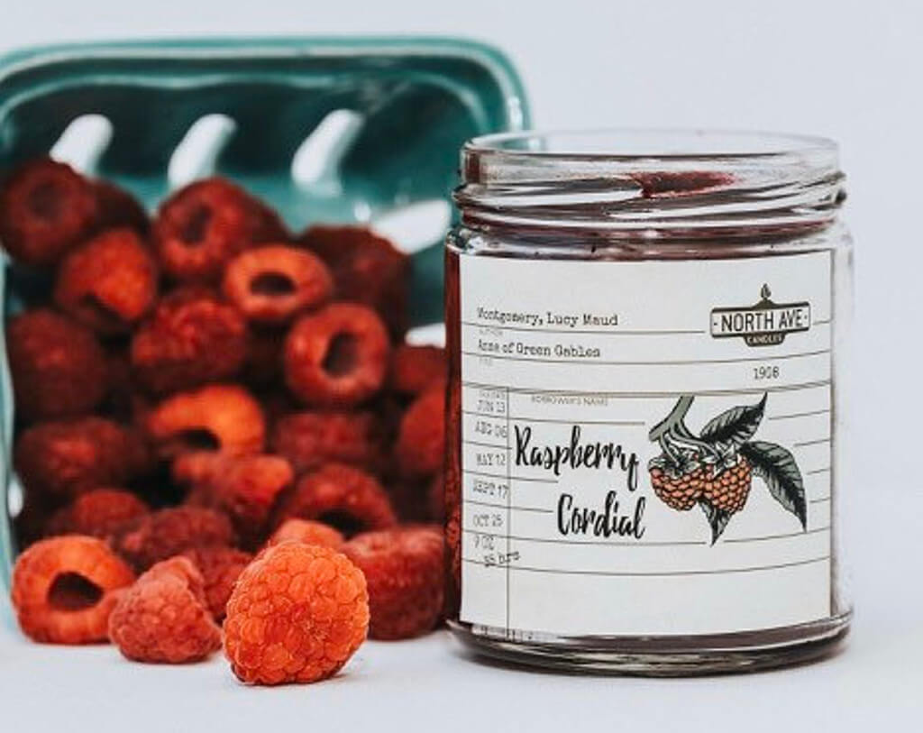 Red Raspberry Cordial candle by North Ave Candles next to fresh raspberries