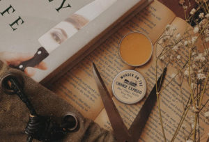 Tin of orange lip balm sitting on top of a book. By Literary Lip Balms