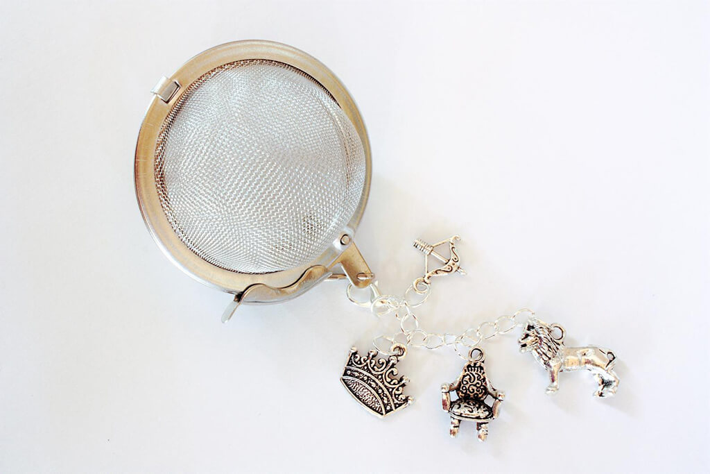 Tea infuser with Narnia-themed charms including a lion, a crown, and a silver chair. By Rosie Lea Tea