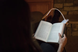 Girl sitting on couch reading a book with a Vont Reading Light