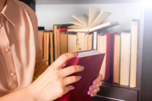 Girl holding a red book and standing in front of a bookshelf