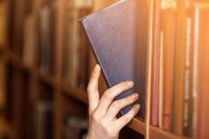 A hand reaching for a blue book on a bookshelf