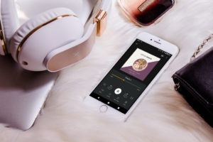 Little women audiobook on phone with headphones and computer sitting nearby