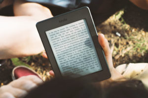 Person reading a book on Kindle while sitting on the lawn