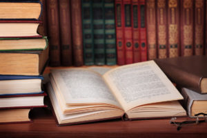 Open book lying on table with stacks of books to the left and behind