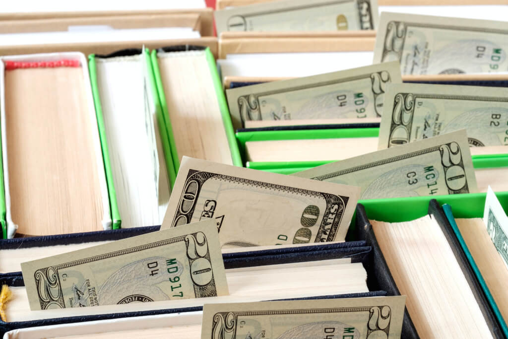 Books stacked next to each other with cash sticking out of the book pages