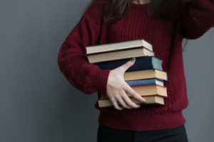 Girl in burgundy sweater holding a stack of books