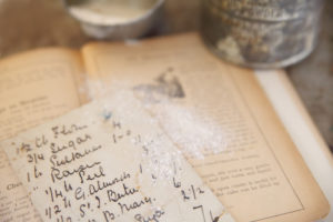 Recipe book laying open with loose recipe on top and flour sprinkled over it
