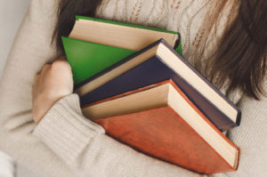 Girl in a beige sweater holding three books in her arms
