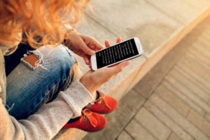Girl with red shoes sitting and reading a book on her phone