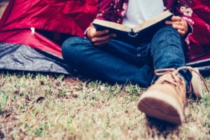 Person reading a book while sitting outside a red tent