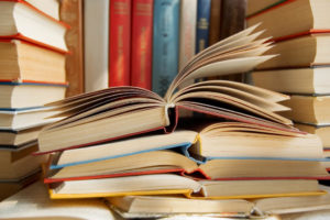 Yellow, red, and blue books opened and stacked up in front of colorful books in a row