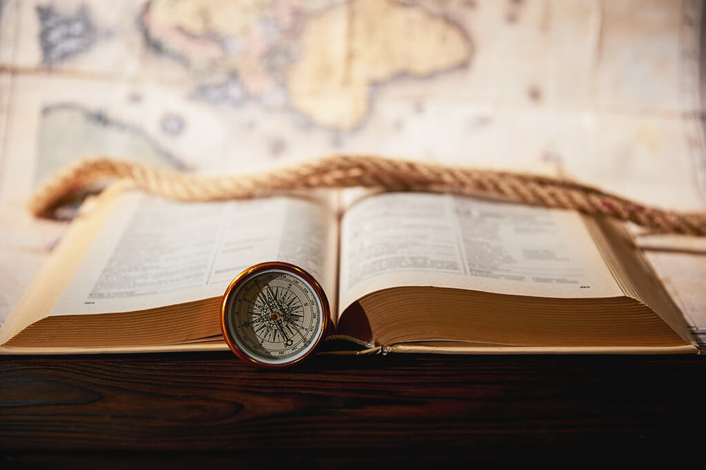 An open book with a compass leaning against it and a map in the background