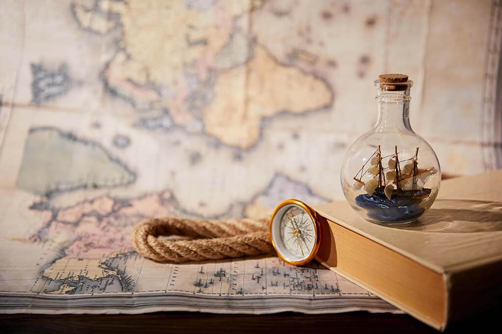 Book, compass, rope, and pirate ship in a bottle sitting on top of a map