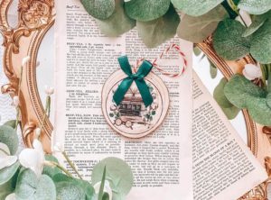 Wood slice ornament with a stack of books burned into the ornament and a green ribbon. By BibliophileTrove