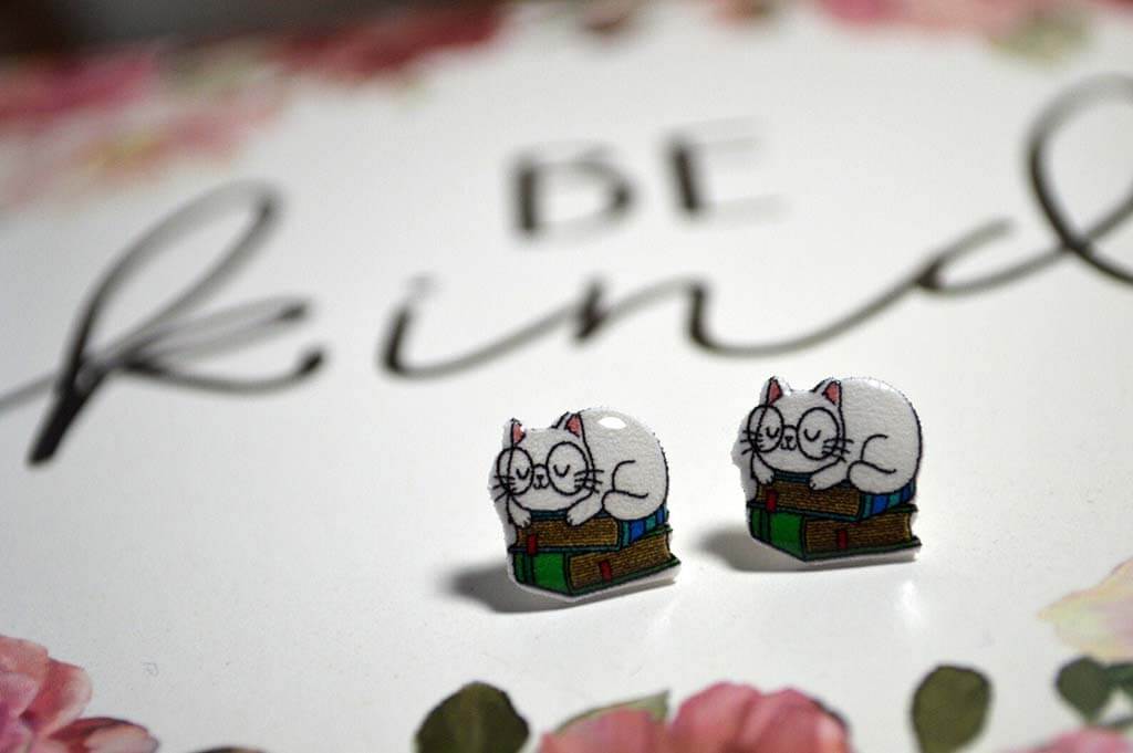 Stud earrings of a white cat sitting on top of a book stack by TheWhimsicalKat