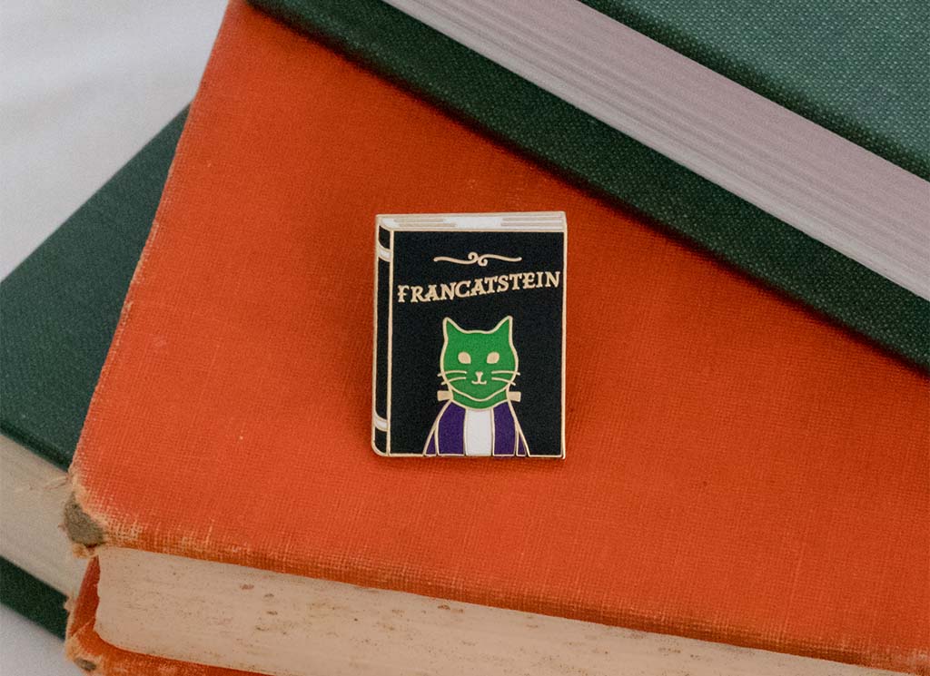 Book shaped enamel pin with the word "Francatstein" and an image of a green cat