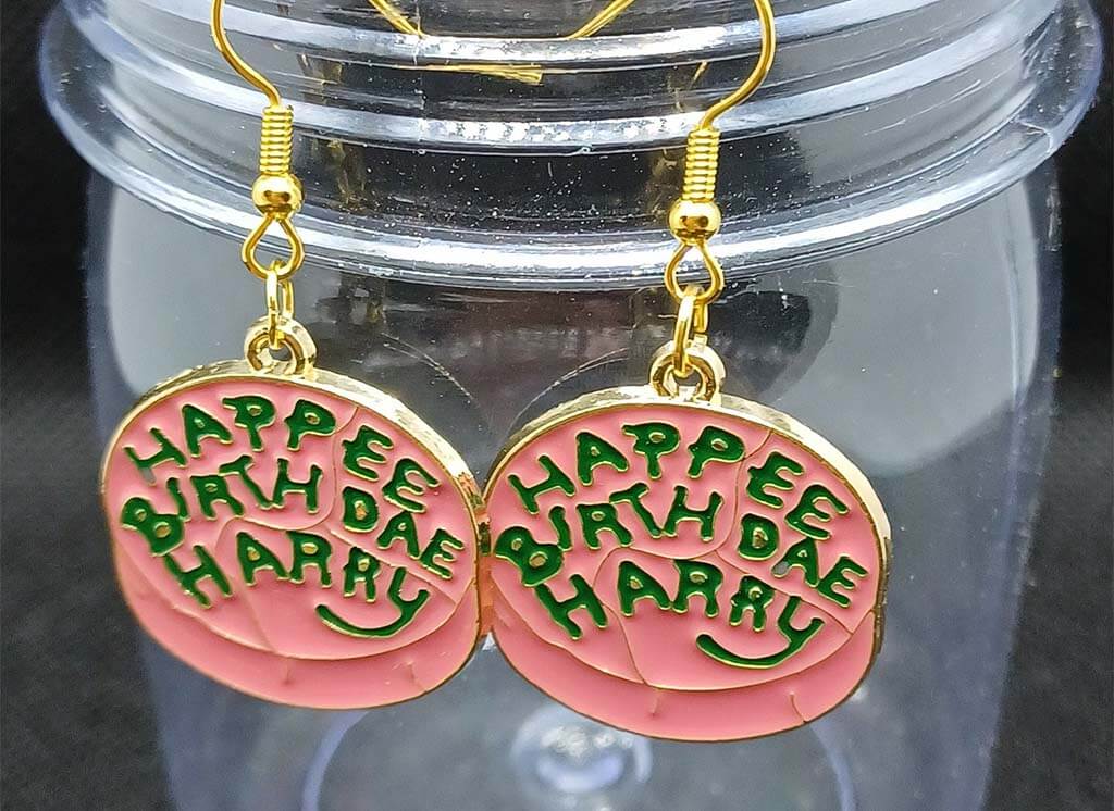 Round earrings that look like pink cake with green frosting that reads "Happee Birthday Harry" by TheMapleLeafMagpie