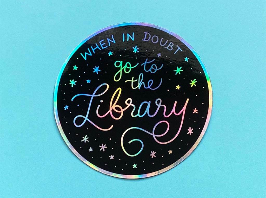 Round holographic sticker with the words "when in doubt, go to the library" by QuillAndBean