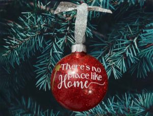 Red glitter ornament with white writing that reads "There's no place like home" by TildyCreations