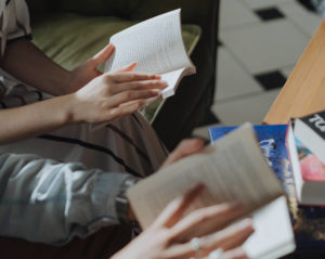 Two people sitting on a couch and holding open books