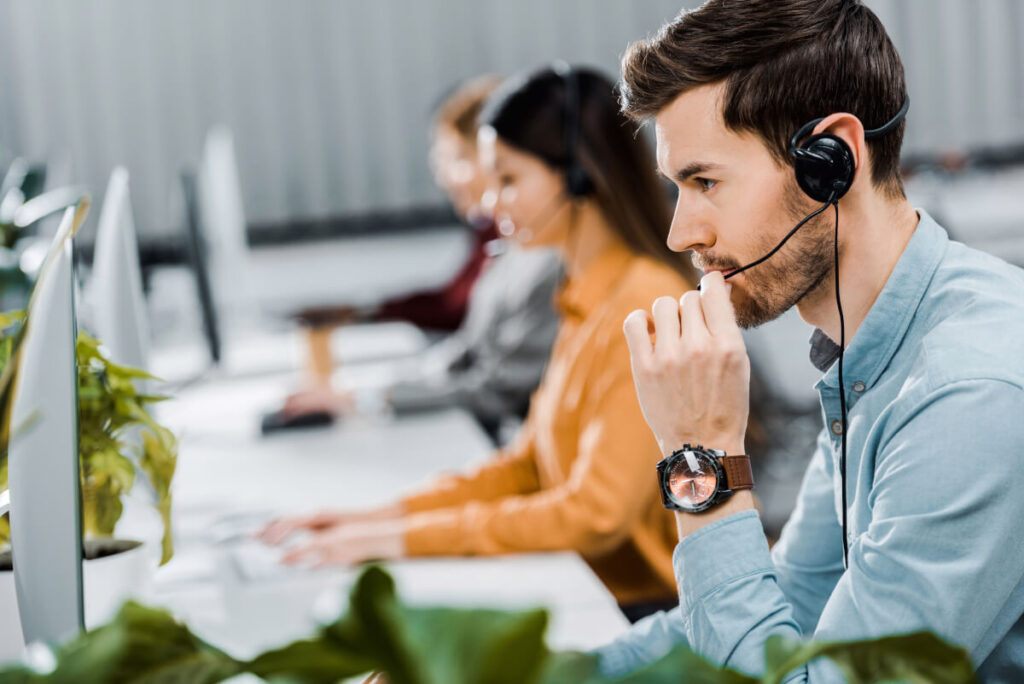 Row of people wearing headsets and working on computers while sitting at a desk