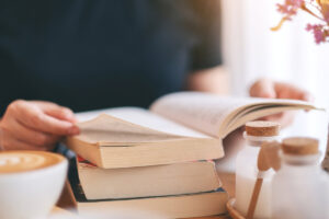 Girl siting and reading with an open book on a desk and coffee next to her
