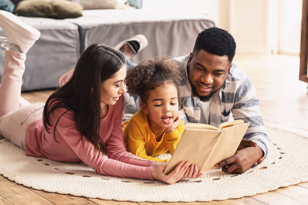 A mom, dad, and child reading a book together on the floor
