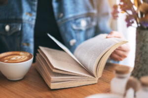 Woman reading an open book on a table with coffee on the left