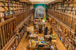 Inside of a London bookstore with an upper floor and wooden railings and bookshelves lining the walls