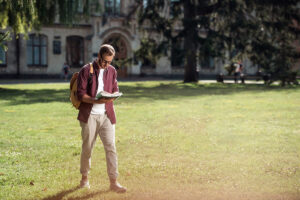 Man walking across grass while reading a book
