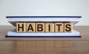 The word "habits" spelled out in wooden blocks and placed inside of a book sitting on a wooden tabletop