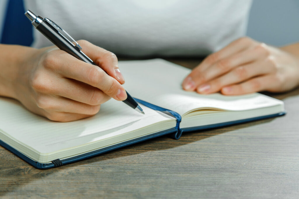 A woman's hands shown as she writes in a blue notebook