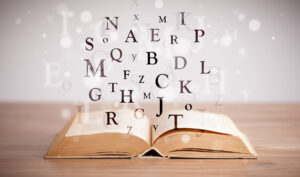 Open book on wood table with letters flying in the air above it