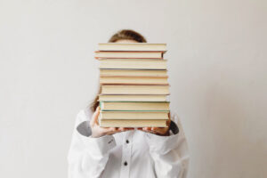 Woman holding a tall stack of books in front of her face