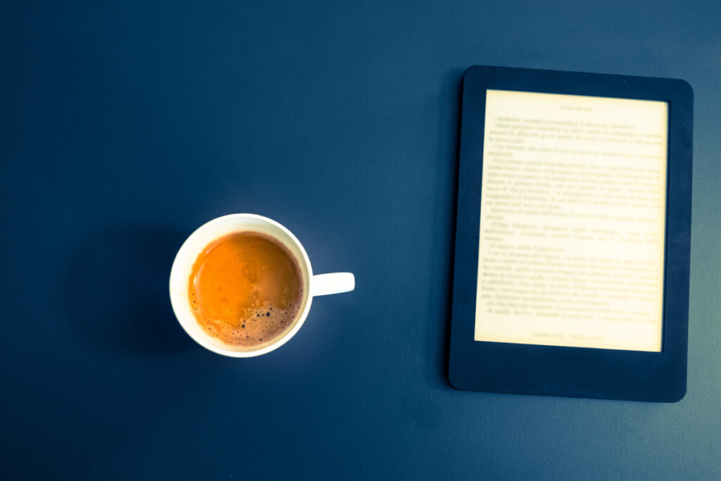 A blue background with a Kindle e-reader on top and a coffee cup on its left